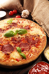 Italian pizza with salami, peperoni - with melted cheese, red tomatoes and green basil on a table decorated by cheese, tomato and cherry tomatoes