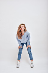 Trying to be funny. Young girl with curious look posing in studio, her hands are on her knees and...