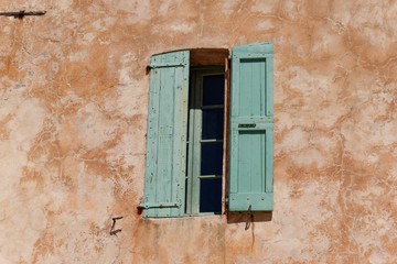 Fototapeta na wymiar Window with wooden green shutters in a terra cotta colored plastered wall, sunny day in april 2017, The Lérins Islands, , France, French Riviera, Provence-Alpes-Cote d'Azur, Europe