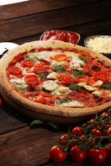Pizza with tomatoes, mozzarella cheese, black olives and basil. Delicious italian pizza on wooden pizza board.