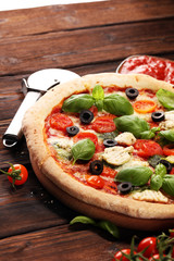 Pizza with tomatoes, mozzarella cheese, black olives and basil. Delicious italian pizza on wooden pizza board.