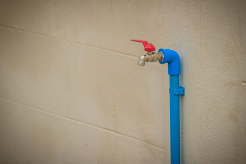 Grungy bronze field faucet connected with blue PVC pipe in white wall background.
