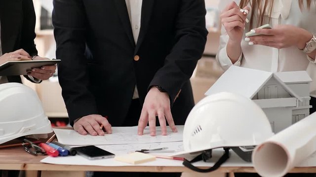 Suits details considering drawing working draft lying on the table, modifying it with a pencil, making notes in Notepad. On the table are glasses, markers and layout