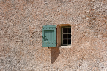 Window with wooden green shutters in a terra cotta colored plastered wall, sunny day in april 2017,...
