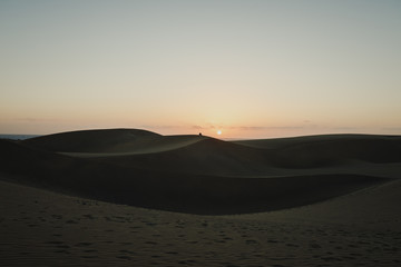 A couple's silhouette sitting on sand during the sunrise in Maspalomas Dunes, Gran Canaria
