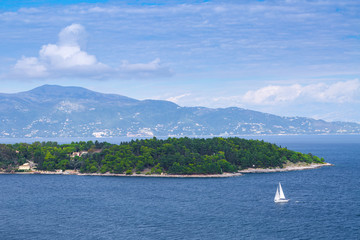 Fototapeta na wymiar Wonderful romantic summertime panoramic seascape. Sailing yacht with white sails in to the crystal clear azure sea. Small green island against coastline slopes.