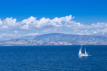 Fototapeta premium Wonderful romantic summertime panoramic seascape. Sailing yacht with white sails in to the crystal clear azure sea against coastline slopes.
