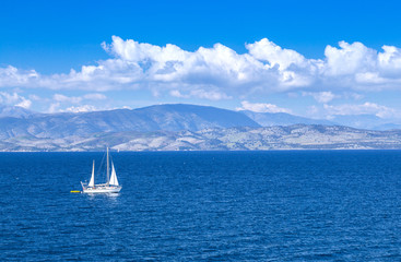 Wonderful romantic summertime panoramic seascape. Sailing yacht with white sails in to the crystal clear azure sea against coastline slopes.