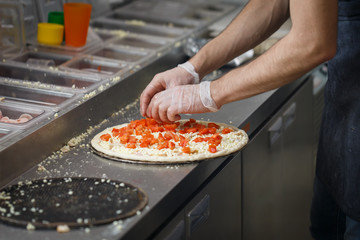 Baker lays tomatoes and cheese on the pizza crust in a fast food restaurant