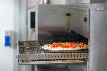 Pizza with stuffing as cheese and tomatoes in the industrial oven at the pizzeria