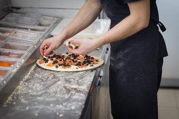 Baker lays the stuffing on the pizza in the fast food restaurant