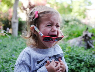 Little girl crying in the garden on spring background. Sad and angry concept.