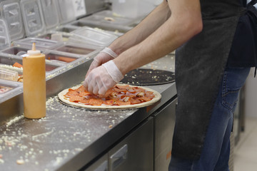 Man lays slices of salami on a pizza