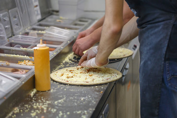 Men make different pizzas in the fast food restaurant