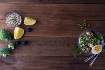Bowl with quinoa and different vegetables - egg, broccoli, tomato, green peas, red onions. Wooden table. Healthy food.