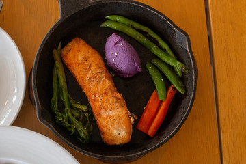 Hot grilled Salmon with mash purple potato and vegetables serve in black plate.