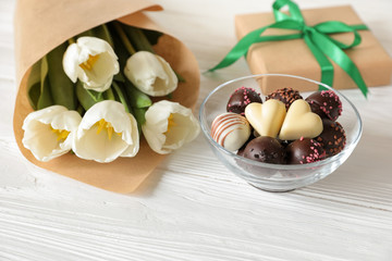 White tulips bouquet, chocolate candies and gift box on white wooden background, spring holidays gift concept.