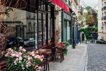 Fototapeta premium Przytulna ulica ze stolikami kawiarni i starego młyna w dzielnicy Montmartre w Paryżu, Francja