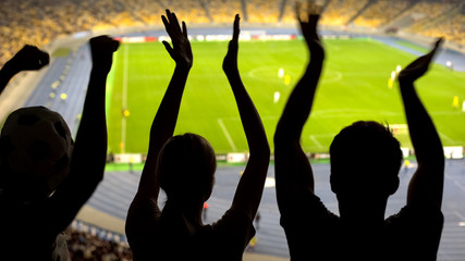 Cheerful soccer fans clapping at crowded stadium, supporting national sport team