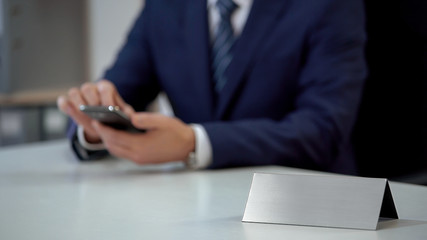 Businessman reading e-mail on smartphone, blank nameplate template for text