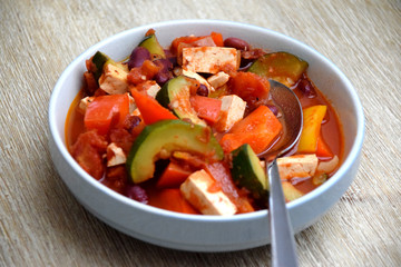 Vegan kidney beans and tofu stew in a blue bowl on wooden table