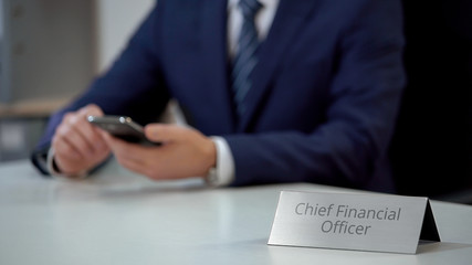 Male chief financial officer texting on smartphone, viewing business files