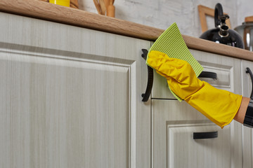 Hands in gloves with green rag is cleaning kitchen cabinets - housework and housekeeping concept