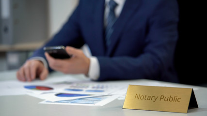 Competent notary public working with documents, checking information on gadget