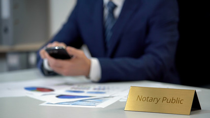 Notary public holding smartphone and working with documents, analyzing data