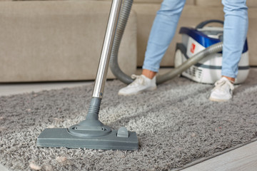 Cropped image of beautiful young woman using a vacuum cleaner while cleaning carpet in the house