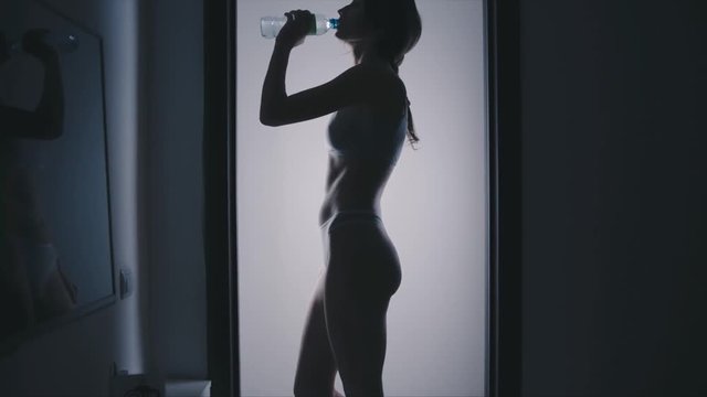 Young fit woman with bottle of water in corridor