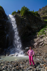 Obraz premium full-length portrait girl in pink pants standing in front of waterfall hands in pockets 