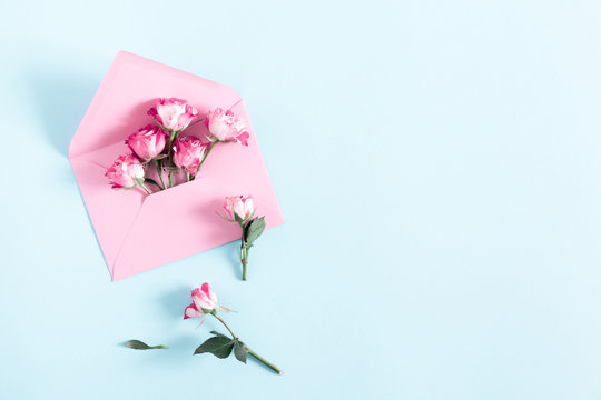 Flowers composition romantic. Pink rose flowers and pink envelopes on pale pastel blue background. Valentine's Day, Easter, Birthday, Happy Women's Day. Flat lay, top view, copy space 
