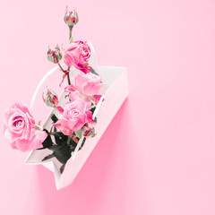 Flowers composition minimal. Pink rose flowers in white paper bag on pastel pink background. Valentine's Day. Birthday, Happy Women's Day. Flat lay, top view, copy space 