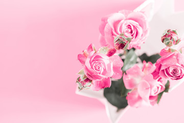 Flowers composition minimal. Pink rose flowers in white paper bag on pastel pink background. Valentine's Day. Birthday, Happy Women's Day. Flat lay, top view, copy space 