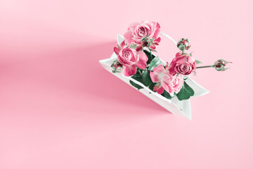 Flowers composition minimal. Pink rose flowers in white paper bag on pastel pink background. Valentine's Day. Birthday, Happy Women's Day. Flat lay, top view, copy space 