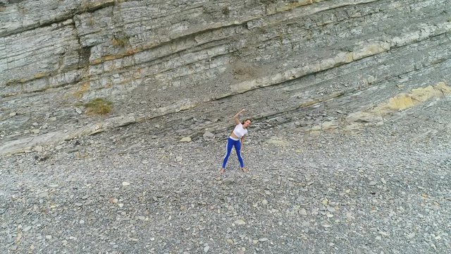 Woman is doing squats the bodyflex during breathing exercises on the rock background. Aerial beautiful footage view.