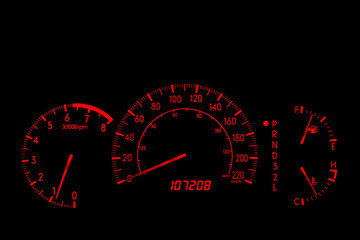 Closeup of an automobile dashboard at night. The dashboard glows orange. There are two speed...