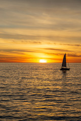 Fototapeta na wymiar A silhouetted sailing boat on the ocean, against a sunset sky