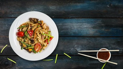 Rotating udon stir fry noodles with seafood and vegetables. Decorated with fresh bean sprouts and chopsticks in a white plate on wooden background. Top view with the copy space for your text
