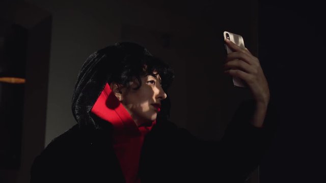 Young, modern, middle eastern woman with black hair and a red sweater playing on her smartphone in a dark setting with beautiful light on her face.