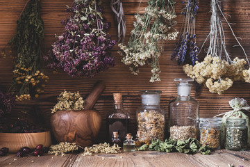 Dried herbs hanging over bottles of tinctures and oils - obrazy, fototapety, plakaty