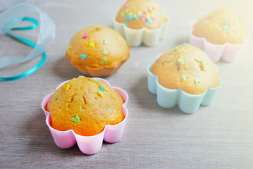Freshly baked muffins with candy sprinkles on white wooden background.