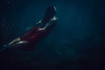 brunette girl in long red dress dives underwater - obrazy, fototapety, plakaty