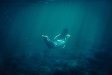 brunette girl in long blue dress floats underwater