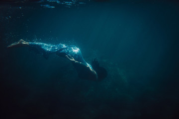 brunette girl in long blue dress swimming underwater - obrazy, fototapety, plakaty