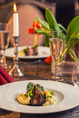 baked beef with baby patizone, sauce and spinach served on white plate with flowers and champagne, romantic time on valentines day