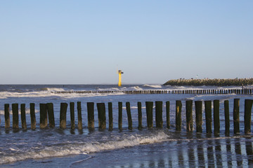 Fototapeta na wymiar row of beach poles and a light house in the sea in holland in winter at a stormy day