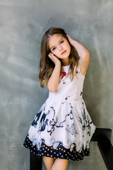 Beautiful little girl with long broun hair and blue eyes sitting on the chair on a grey background...