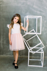 Beautiful little girl with broun long hair on a grey background near the white constructure of the cubes